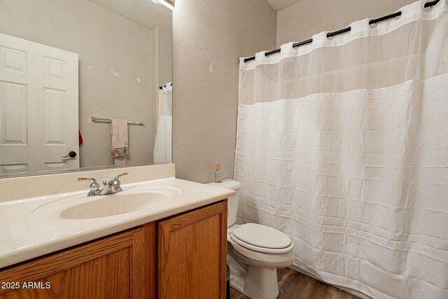 bathroom with toilet, vanity, a textured wall, and wood finished floors