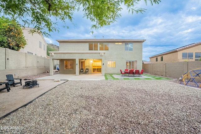 rear view of property with stucco siding, a patio, a fire pit, and a fenced backyard