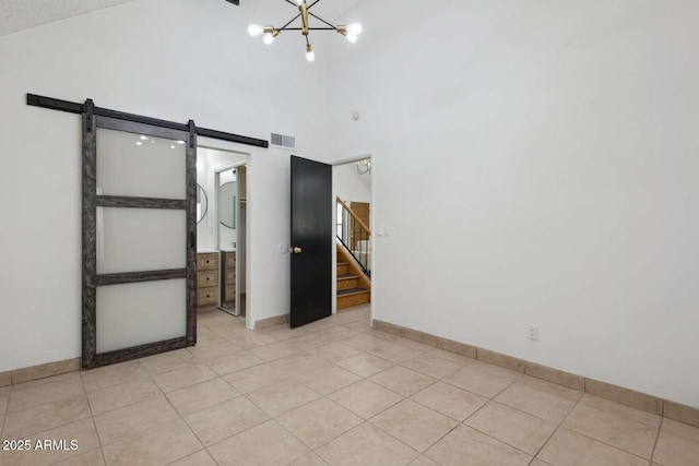 tiled empty room featuring high vaulted ceiling, a barn door, and a chandelier