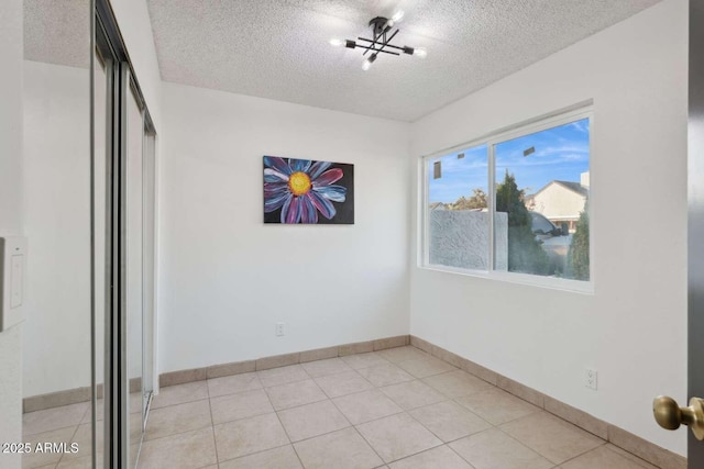 tiled empty room featuring an inviting chandelier and a textured ceiling