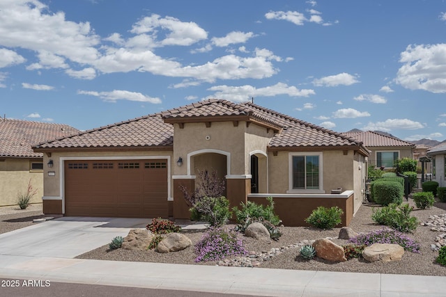 mediterranean / spanish home featuring a garage, stucco siding, a tiled roof, and concrete driveway