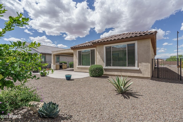 rear view of property featuring fence, stucco siding, a gate, a patio, and a tiled roof