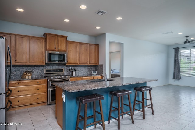 kitchen featuring brown cabinetry, visible vents, tasteful backsplash, a sink, and stainless steel appliances