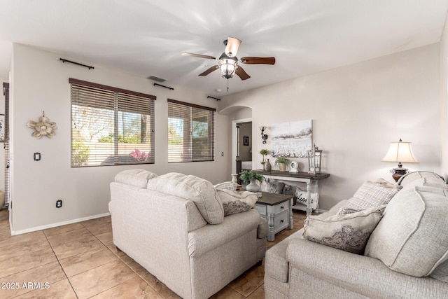 living room featuring light tile patterned floors, baseboards, visible vents, arched walkways, and a ceiling fan