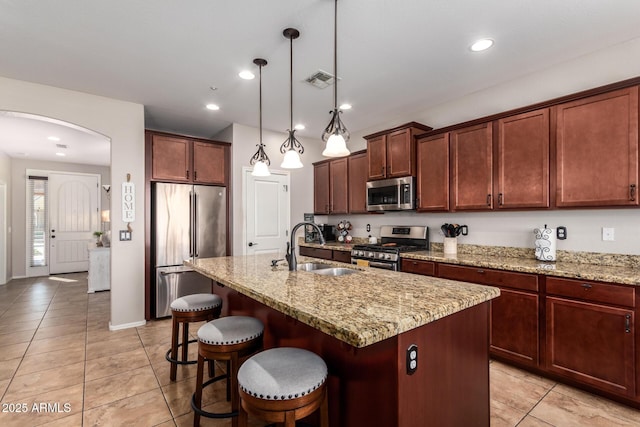 kitchen with stainless steel appliances, a sink, a center island with sink, and pendant lighting