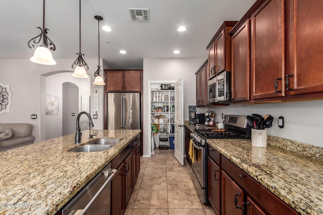 kitchen with arched walkways, decorative light fixtures, stainless steel appliances, visible vents, and a sink