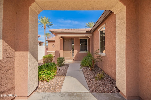 view of exterior entry with a tile roof and stucco siding