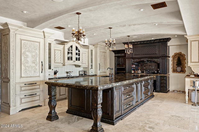 kitchen with dark stone countertops, cream cabinets, an inviting chandelier, a large island with sink, and sink