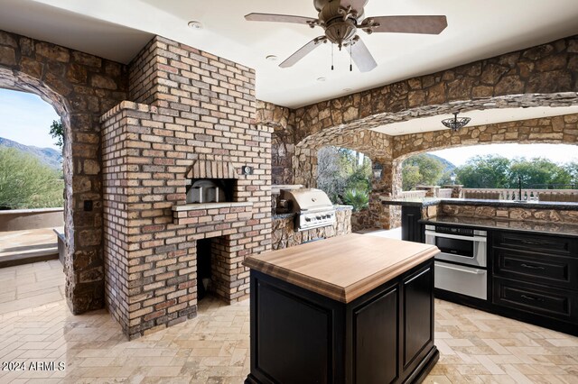 exterior space with an outdoor brick fireplace, butcher block counters, a center island, ceiling fan, and stainless steel oven