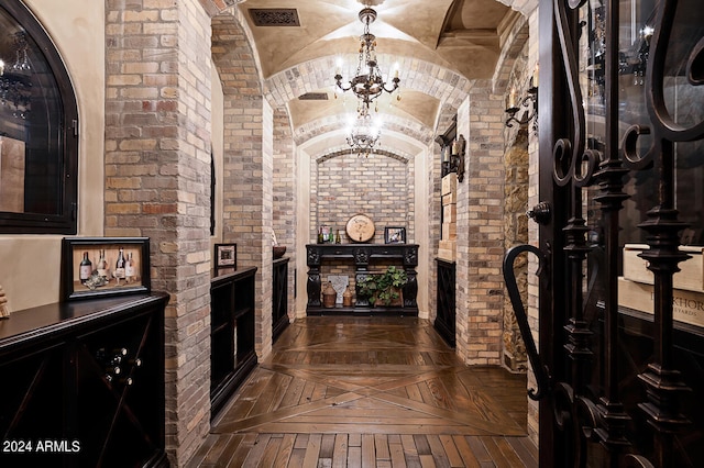 wine cellar featuring dark parquet floors, vaulted ceiling, a chandelier, and brick wall