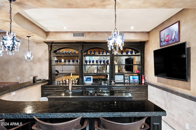 bar with dark stone countertops and an inviting chandelier