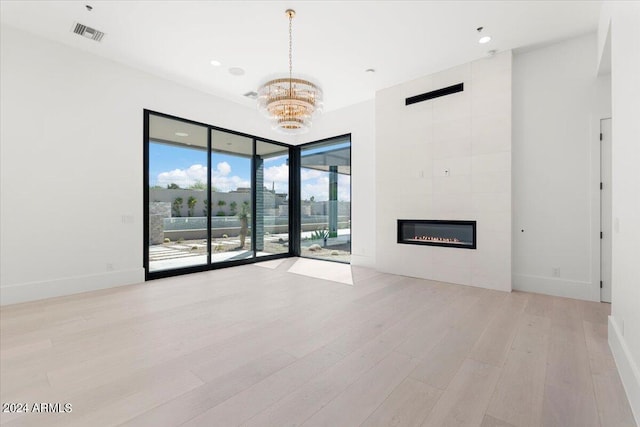 unfurnished living room featuring a notable chandelier, a healthy amount of sunlight, a fireplace, and light hardwood / wood-style flooring