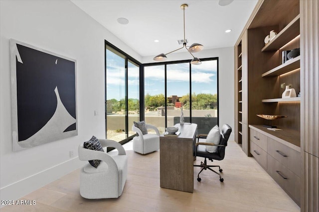 office with plenty of natural light, light hardwood / wood-style floors, built in shelves, and an inviting chandelier