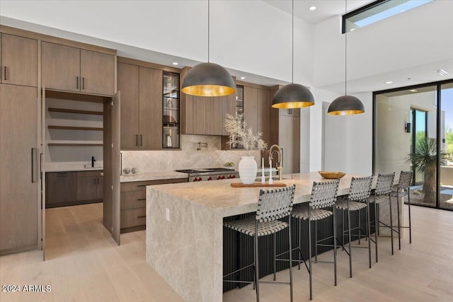 kitchen featuring backsplash, a center island with sink, light wood-type flooring, and pendant lighting