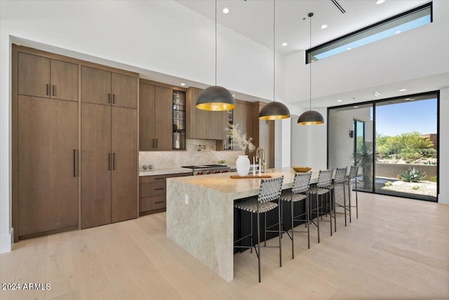 kitchen with light hardwood / wood-style floors, a kitchen breakfast bar, a large island, backsplash, and pendant lighting