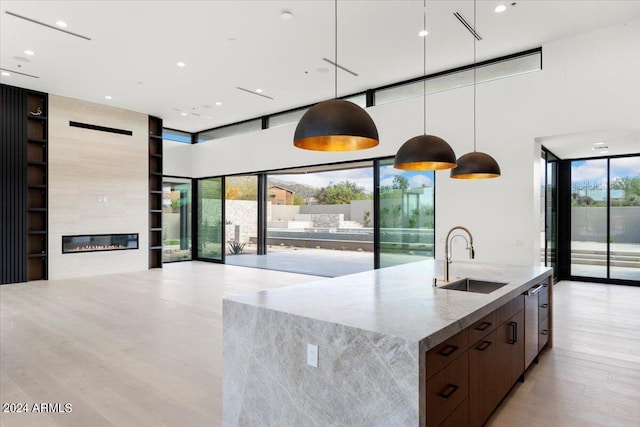 kitchen featuring light hardwood / wood-style flooring, a large fireplace, a wall of windows, decorative light fixtures, and sink