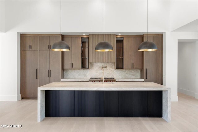 kitchen featuring light hardwood / wood-style flooring, hanging light fixtures, tasteful backsplash, a kitchen island with sink, and a high ceiling