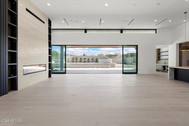 unfurnished living room with a towering ceiling, built in shelves, a large fireplace, and light wood-type flooring