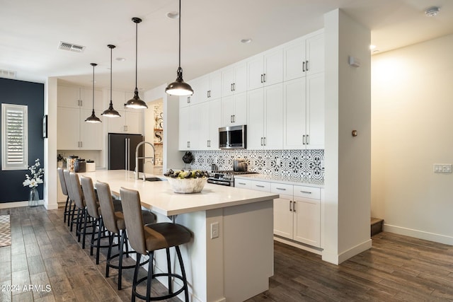 kitchen featuring appliances with stainless steel finishes, an island with sink, hanging light fixtures, and white cabinets