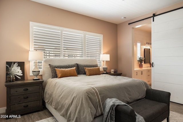 bedroom featuring a barn door, hardwood / wood-style floors, and ensuite bath