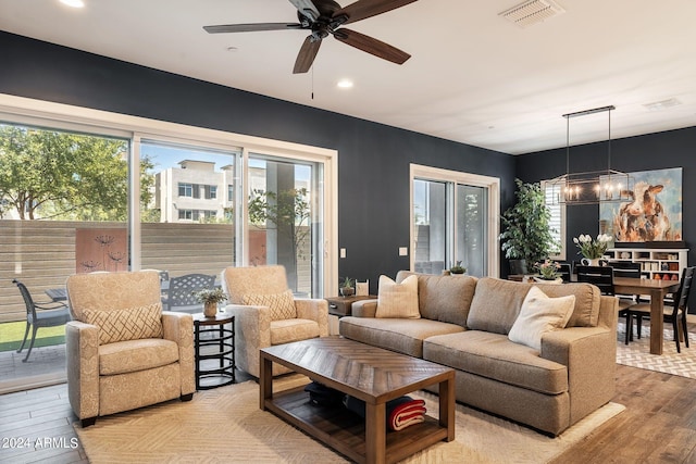 living room with ceiling fan with notable chandelier and light wood-type flooring