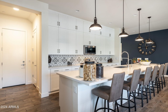 kitchen featuring pendant lighting, sink, dark hardwood / wood-style flooring, decorative backsplash, and a center island with sink