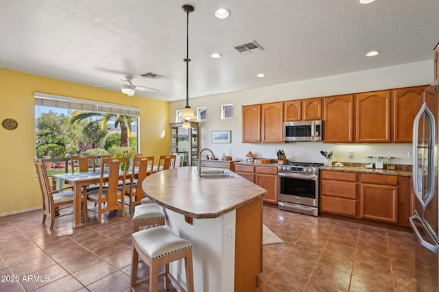 kitchen featuring brown cabinetry, visible vents, stainless steel appliances, and a sink