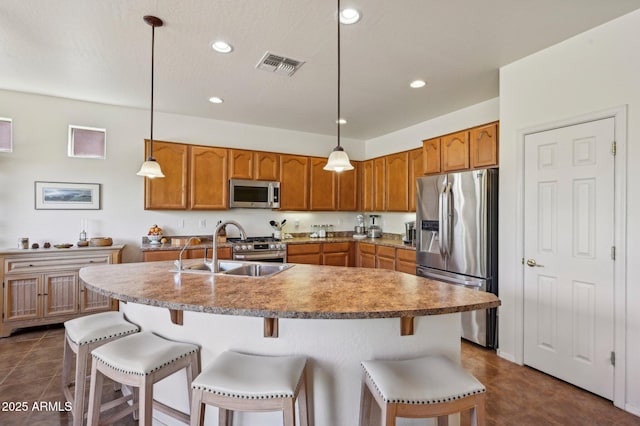 kitchen with visible vents, a breakfast bar area, appliances with stainless steel finishes, brown cabinets, and a sink