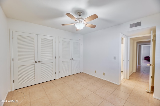 unfurnished bedroom with light tile patterned floors, two closets, and ceiling fan