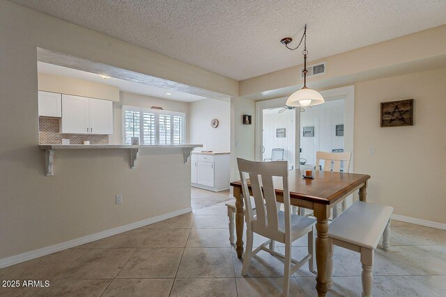 dining area featuring light tile patterned floors, a textured ceiling, visible vents, and baseboards