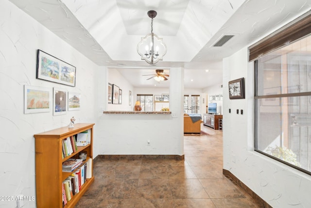 hallway with a raised ceiling, dark tile patterned floors, and an inviting chandelier