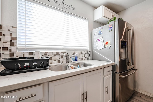 kitchen with sink, decorative backsplash, stainless steel fridge, light stone countertops, and white cabinetry