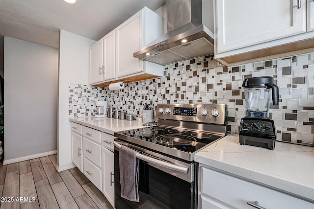 kitchen with stainless steel range with electric stovetop, backsplash, white cabinets, wall chimney exhaust hood, and light stone countertops