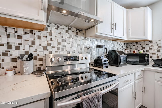 kitchen with tasteful backsplash, light stone counters, stainless steel range with electric stovetop, wall chimney range hood, and white cabinetry