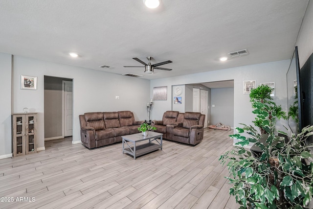 living room featuring ceiling fan, a textured ceiling, and light wood-type flooring