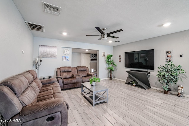 living room featuring ceiling fan, light wood-type flooring, and a textured ceiling