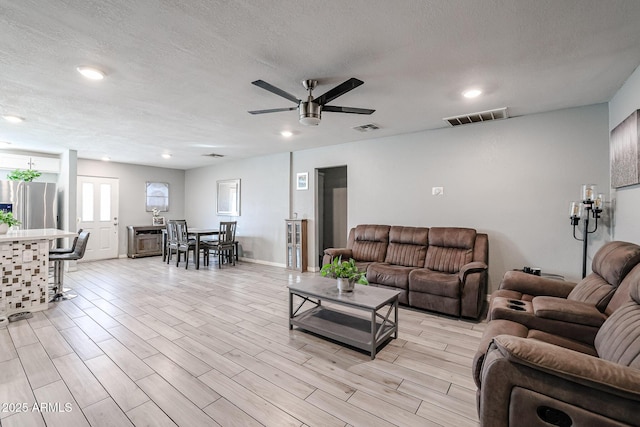 living room with light wood-type flooring, a textured ceiling, and ceiling fan