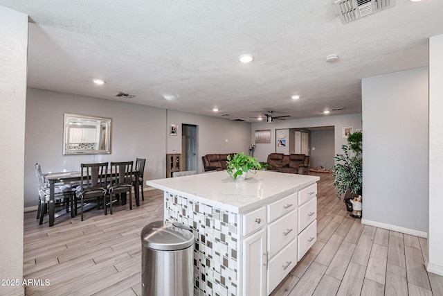 kitchen with a textured ceiling, a kitchen island, ceiling fan, light hardwood / wood-style floors, and white cabinetry