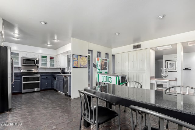 kitchen featuring appliances with stainless steel finishes, white cabinetry, dark stone counters, and sink