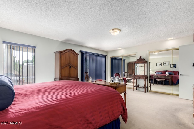 bedroom with a textured ceiling, light carpet, and multiple closets