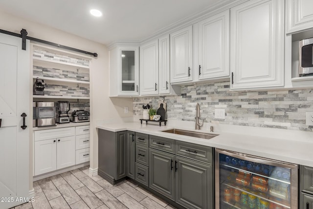 kitchen with beverage cooler, a sink, white cabinets, decorative backsplash, and gray cabinets