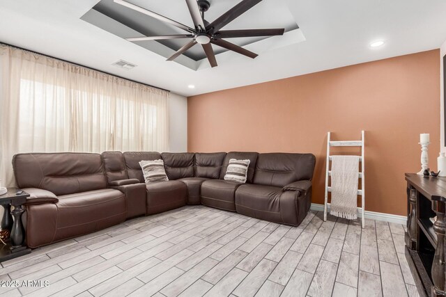 living area with a ceiling fan, a raised ceiling, light wood-style flooring, baseboards, and recessed lighting