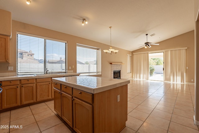 kitchen featuring vaulted ceiling, a tile fireplace, light tile patterned floors, a center island, and tile counters