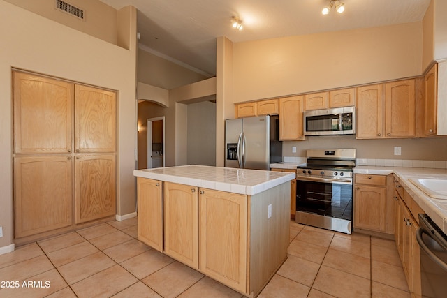 kitchen with tile countertops, a center island, light tile patterned floors, light brown cabinetry, and stainless steel appliances