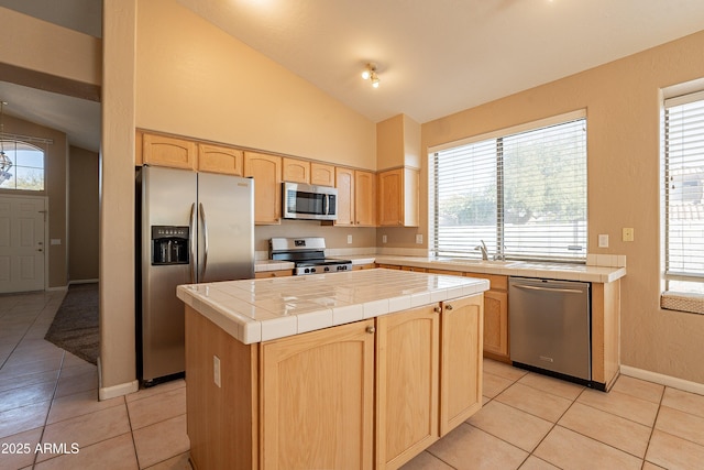 kitchen with appliances with stainless steel finishes, light tile patterned floors, a center island, tile counters, and lofted ceiling