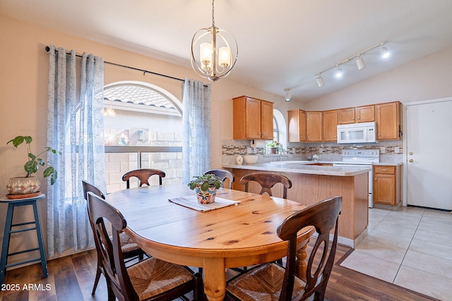 dining space with light hardwood / wood-style floors, lofted ceiling, and an inviting chandelier