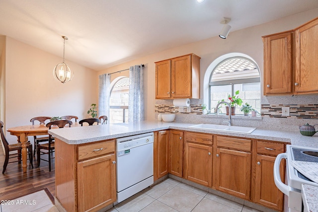 kitchen with kitchen peninsula, tasteful backsplash, decorative light fixtures, dishwasher, and sink