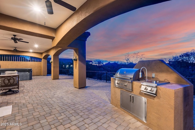 patio terrace at dusk with ceiling fan, an outdoor kitchen, and grilling area