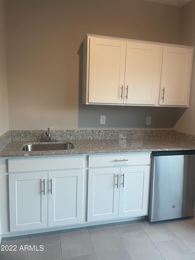 kitchen with a sink, light stone countertops, stainless steel dishwasher, light tile patterned floors, and white cabinets