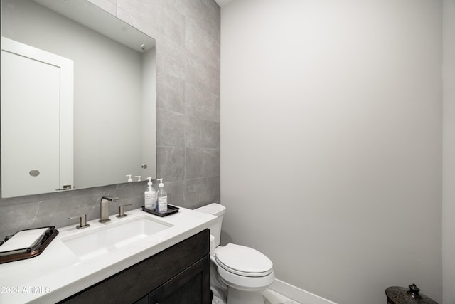 half bathroom with toilet, tasteful backsplash, vanity, and tile walls